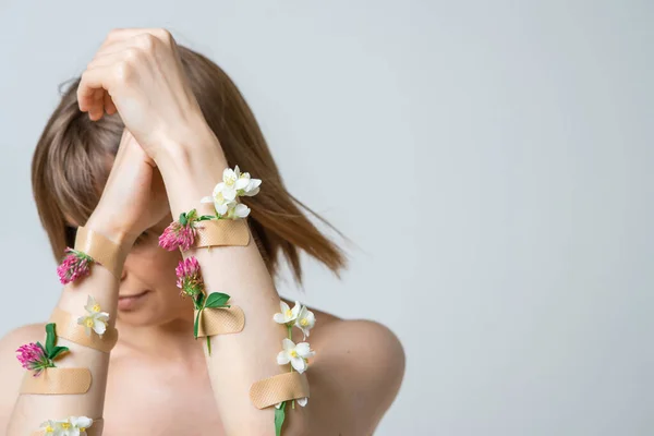 Young girl turning face away from camera with hands with flowers and plasters, concept photo for feminist or beauty blog
