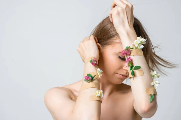 Pretty young woman covering face with hands with flowers and plasters, concept photo for feminist or beauty blog