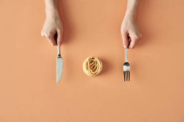 Makaron Fettuccine, widelec i nóż w dłoniach izolowane na beżowym tle, minimalistyczna fotografia na blogu żywności lub reklamy — Zdjęcie stockowe