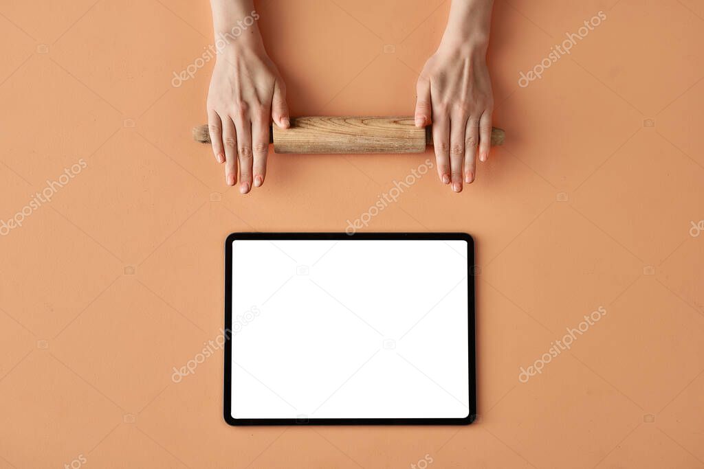 Rolling pin for dough in hands and tablet with copy space on beige background, conceptual photo for food blog or ad