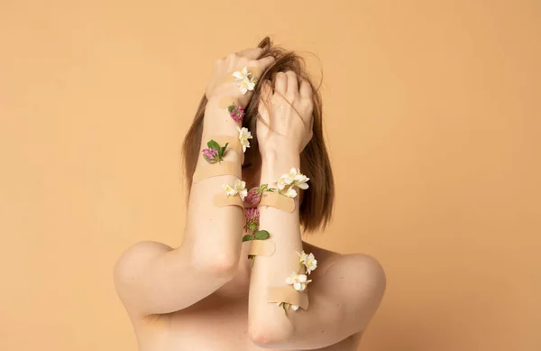 Pretty young girl covering face with hands with flowers and plasters, concept photo for feminist or beauty blog