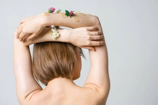 Dos de jolie femme avec des mains avec des fleurs et des taches sur fond blanc, concept photo pour blog féministe ou beauté — Photo