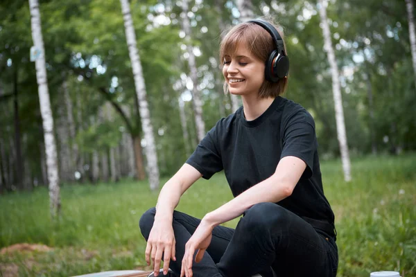 Pretty teen girl in wireless headphones listening to music and meditating in the park, photography for ad or blog