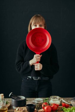 Sevimli genç bir kız sıcak bir mutfakta yemek pişiriyor. Siyah arka planda. Yaşam tarzı yemek blogu içeriği. Sağlıklı beslenme.