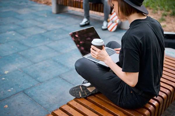 Kreatív fiatal lány kalap blogger munka laptop ül padon egy csésze kávé skatepark, kilátás hátulról — Stock Fotó