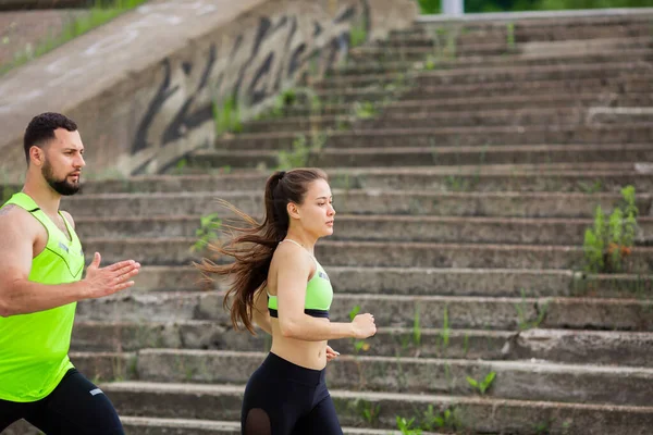 Молодая пара в стильной спортивной одежде работает на фоне лестницы, бег соревнования, спорт и здоровый образ жизни — стоковое фото