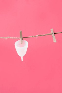 Adet bardağı beyaz çevre dostu pembe arka planda izole edilmiş çamaşır ipinde asılı, kadın blogu için fotoğraf veya reklam afişi