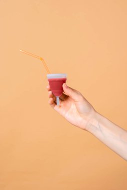 Regl sıvısı ve elinde tüp bulunan regl bardağı bej arka planda, kadınlar için konsept fotoğraf veya feminist blog