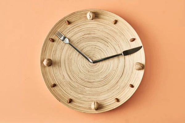 Fındık, çatal ve bıçaktan yapılmış mutfak saati bej arka planda izole edilmiş, sağlıklı yemek blogu için kavramsal fotoğrafçılık