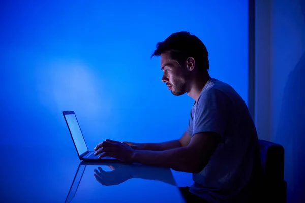 Hacker megpróbálja feltörni a biztonsági rendszert, hogy ellopja a fontos vállalati információkat, dolgozik laptop kék neon fény — Stock Fotó
