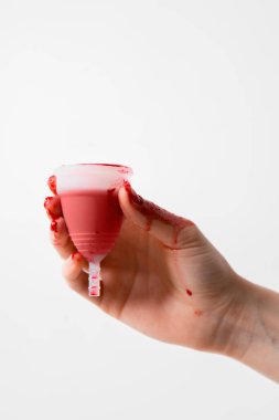 Regl bardağı yeniden kullanılabilir ve silikonlu. Beyaz bir arka planda izole edilmiş adet sıvısı olan kadın eli.