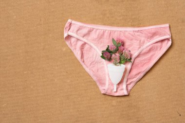 Regl bardağı yeniden kullanılabilir. Bej arka planda izole edilmiş kadın iç çamaşırlarında çiçekler var.