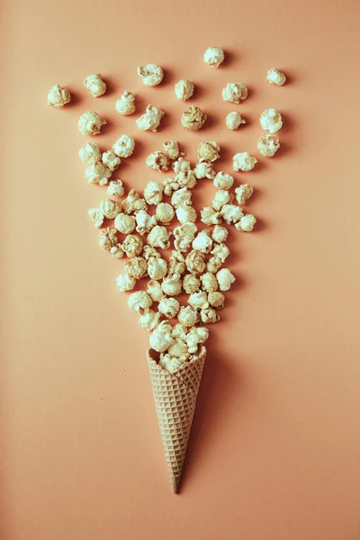 Popcorn spills out of waffle cone on beige background, snack, concept flat lay photography and content for food blog — Stock Photo, Image