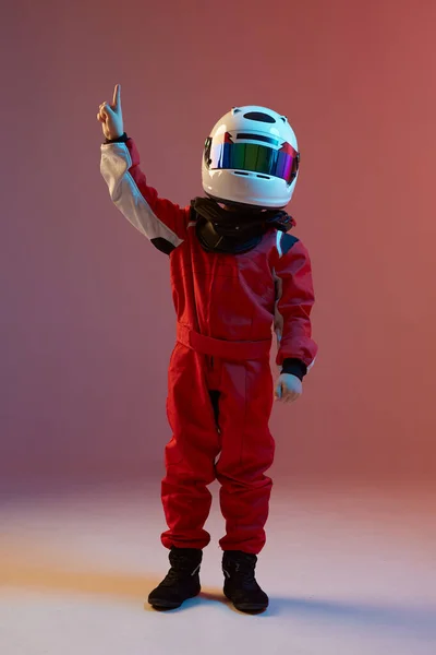 Мальчик-гонщик в шлеме с поднятой рукой, стоящий в неоновом свете. Плакат школы картинга — стоковое фото