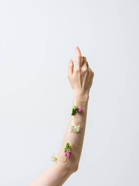 Womans hand raised up with patches and flowers isolated on white, concept photography for beauty or feminist blog.