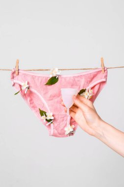 Kadınlarda yeniden kullanılabilen bir adet bardağı. Beyaz arka planda saklanmış çiçekli kadın iç çamaşırları.
