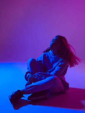 Şık bir genç kız, havalı bir kapüşonlu poz, saçları uzamış, neon arka planda. Dans okulu posteri