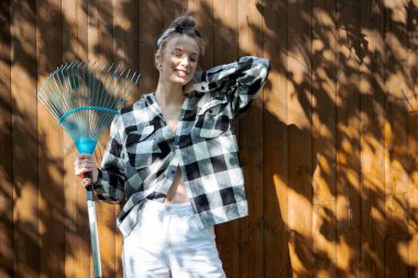 Elinde tırmıkla bahçedeki ahşap çitin arkasında duran genç ve güzel bir kız..