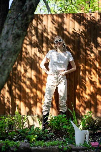 Retrato de una chica bonita con gafas y un pañuelo en la cabeza de pie contra una valla de madera en el patio trasero en un día soleado . —  Fotos de Stock
