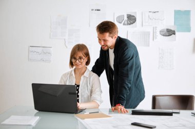 Mimarlardan oluşan yaratıcı bir ekip gülümseyen kız ve erkek fikirleri tartışıyor, modern ofiste dizüstü bilgisayarla çalışıyorlar.