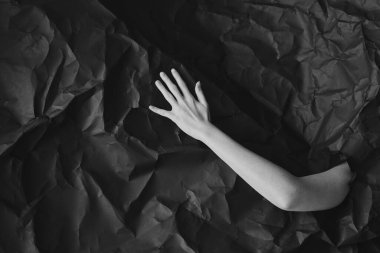 Kadın eli siyah buruşuk kağıtta, siyah beyaz konsept fotoğrafçılıkta güzellik blogu veya poster için delikten çıkar.