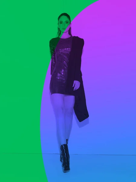 Pretty young woman in disco clothes in a short dress on neon green violet background. Photography for ad or blog