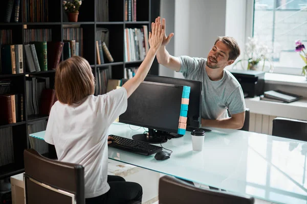 Young designers or programmers girl and guy work at computers in office, give each other a high five