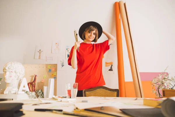 Young pretty girl artist in hat stands with brushes in art studio. Photo for advertising courses illustrations or blog