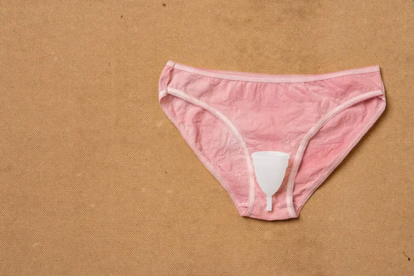 Menstruationstasse umweltfreundlich weiß und wiederverwendbar auf Damenunterwäsche isoliert auf beigem Hintergrund — Stockfoto