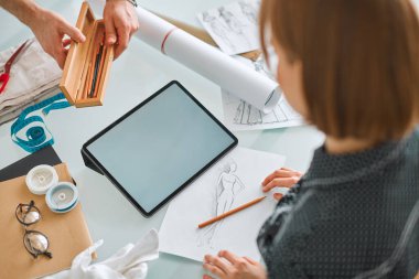 Güzel kız moda tasarımcısı atölyede boş ekranla tablet üzerinde çalışıyor. Reklam kursları veya kıyafetler için fotoğraf