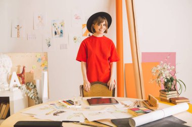 Sanat stüdyosunda şapka giyerken gülümseyen genç bir sanatçı kız çizer. Reklam sanatı kursları veya blog için fotoğraf