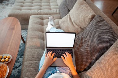 Genç kız boş ekran laptopuyla kanepede uzanıp rahat atmosferde dizileri seyrediyor. Reklam veya blog için fotoğrafçılığı kapat