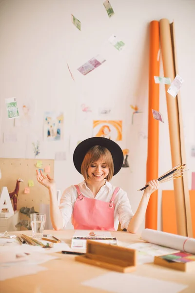 Ilustradora chica sonriente creativa sentada bajo la lluvia de dinero en el taller. Concepto foto sobre arte y freelance — Foto de Stock