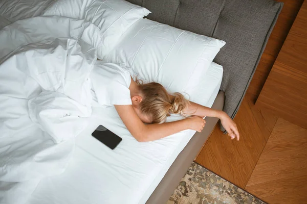 Niña dormir con teléfono bajo manta en cama blanca en el dormitorio. Sueño saludable, aplicaciones de sueño saludable, adicción a Internet — Foto de Stock