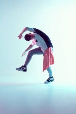Stüdyoda çağdaş dans eden adam. Neon açık mavi arka plan. Akrobatik bboy dansçısı. Break dans dersleri.