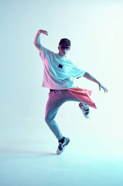 Stüdyoda çağdaş dans eden adam. Neon açık mavi arka plan. Akrobatik bboy dansçısı. Break dans dersleri.