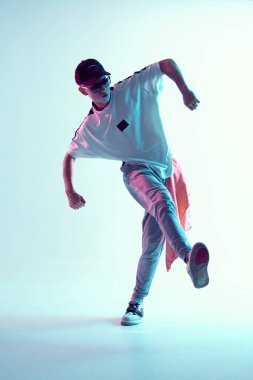 Stüdyoda çağdaş dans eden adam. Neon açık mavi arka plan. Akrobatik bboy dansçısı. Break dans dersleri.