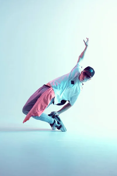 Guy dancing contemporary dance in studio. Neon light blue background. Acrobatic bboy dancer. Break dance lessons.