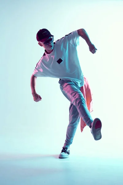 Guy dancing contemporary dance in studio. Neon light blue background. Acrobatic bboy dancer. Break dance lessons.