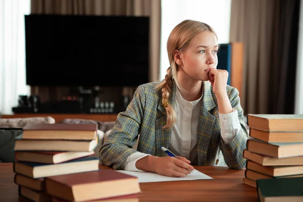 Fiatal aranyos gondolkodó tini lány diák ül könyvek az asztalnál az osztályteremben vagy a könyvtárban. Vissza az iskolába. — Stock Fotó