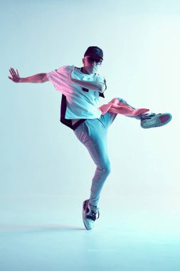Stüdyoda çağdaş dans eden adam. Neon açık mavi arka plan. Akrobatik bboy dansçısı. Break dans dersleri.