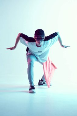 Stüdyoda çağdaş dans eden adam. Neon açık mavi arka plan. Akrobatik bboy dansçısı. Break dans dersleri.