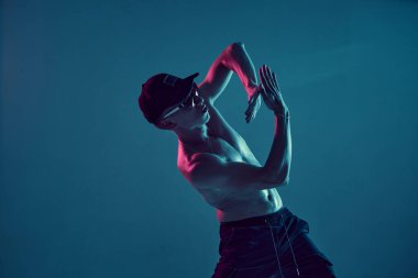Şapkalı ve güneş gözlüklü adam neon mavi ışıkta hip-hop yapıyor. Dans okulu posteri