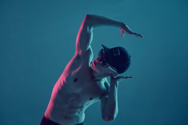 Şapkalı ve güneş gözlüklü genç adam stüdyo mavi ışıkta tişörtsüz break dans yapıyor. Break dans dersleri