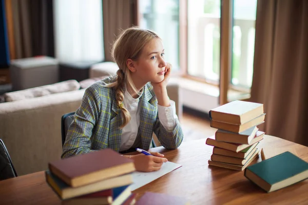 Fiatal aranyos gondolkodó tini lány diák ül könyvek asztalnál osztályteremben vagy könyvtárban. Vissza az iskolába. — Stock Fotó