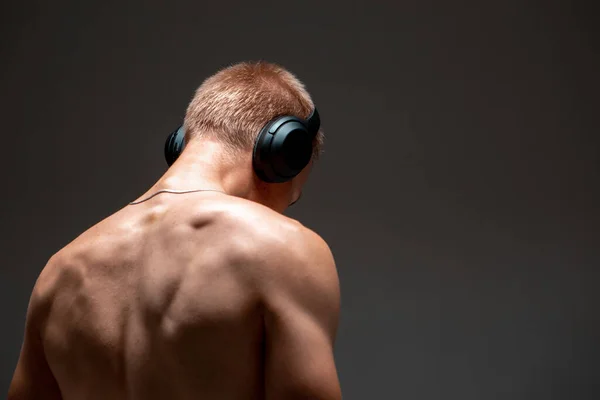 Fiatal srác vezeték nélküli fejhallgatóval zenét hallgat ing nélkül a stúdióban. Zenés poszter. Kilátás hátulról — Stock Fotó