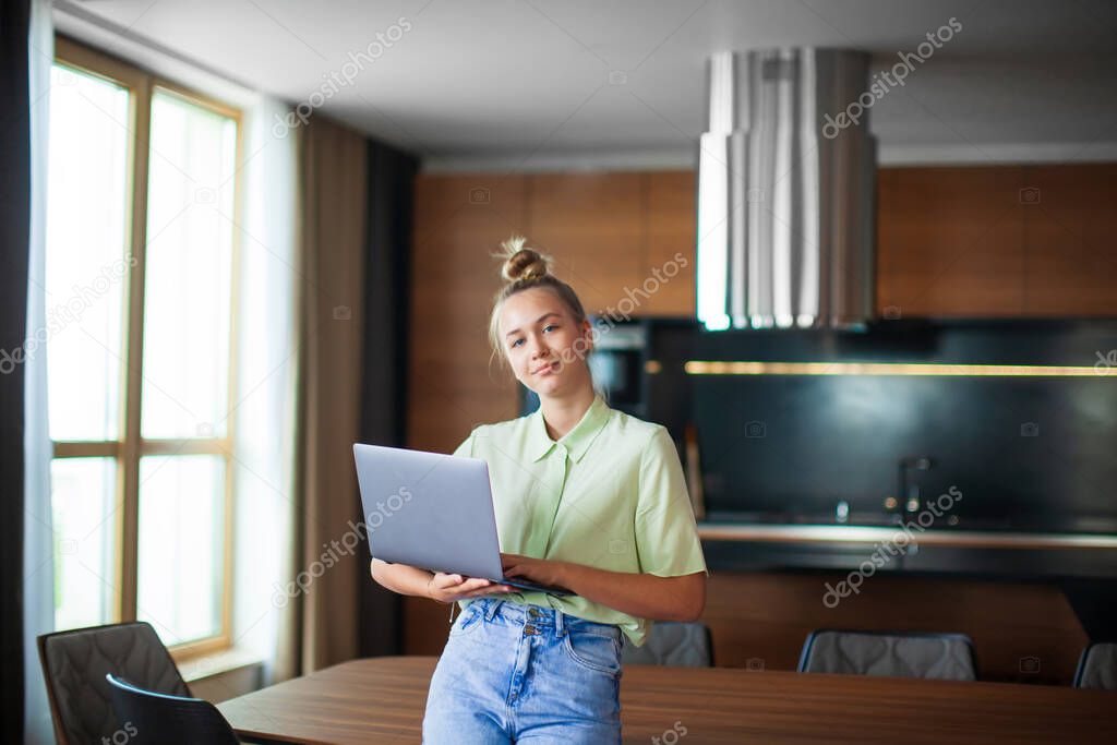 Creative young girl blogger with laptop stands at home office. Cozy home environment