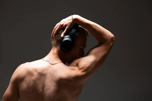 Il ragazzo figo con le cuffie wireless ascolta una canzone senza camicia in studio. Manifesto musicale. Vista dal retro — Foto Stock