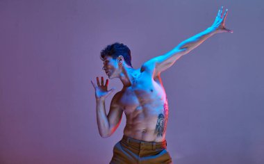 Havalı genç adam neon ışıkta gömleksiz dans ediyor. Renkli dans okulu posteri. Dövmeli vücut..