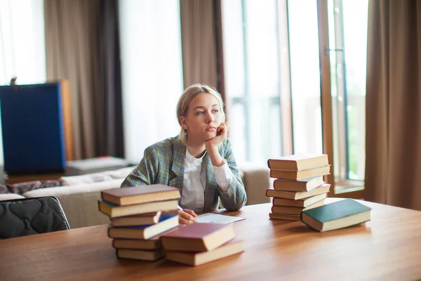 Fiatal aranyos gondolkodó tini lány diák ül könyvek asztalnál osztályteremben vagy könyvtárban. Vissza az iskolába. — Stock Fotó